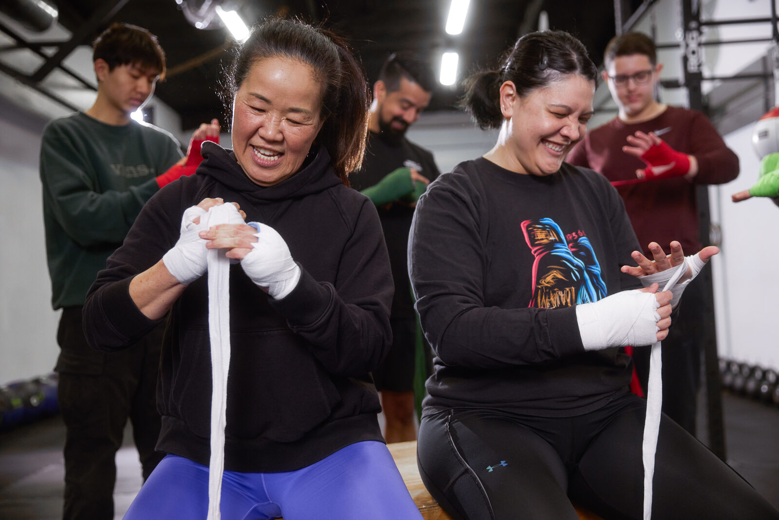 Two students laughing together while wrapping hands for boxing